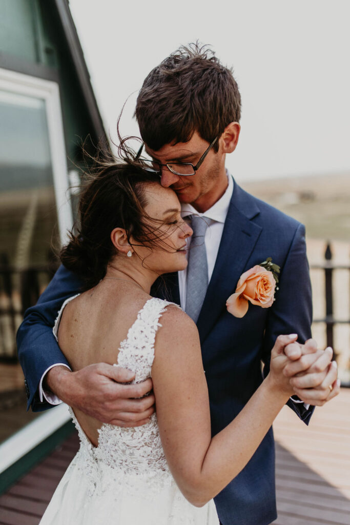 Close-up of bride and groom dancing with wind in their hair during their outdoor wedding, groom wearing a suit with a peach rose boutonniere

