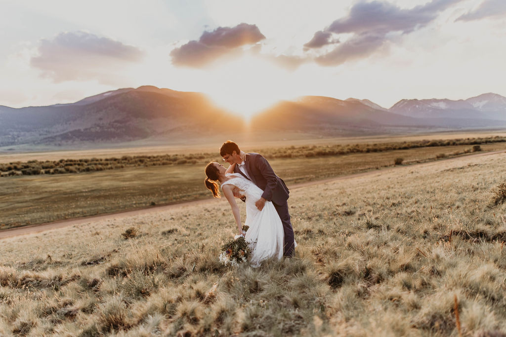 Groom dips bride at sunset in a wide open mountain field, golden light spilling across the grass during a romantic Norway couple photoshoot