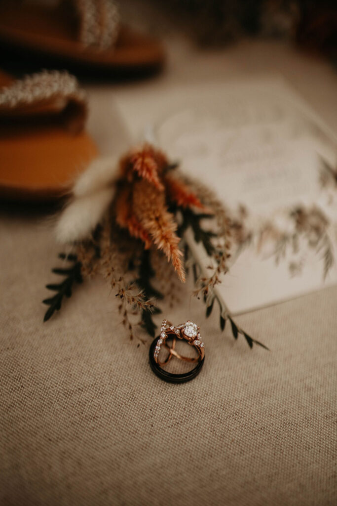 Flat lay of wedding rings styled with dried florals, soft earthy tones and detail invitation in the background

