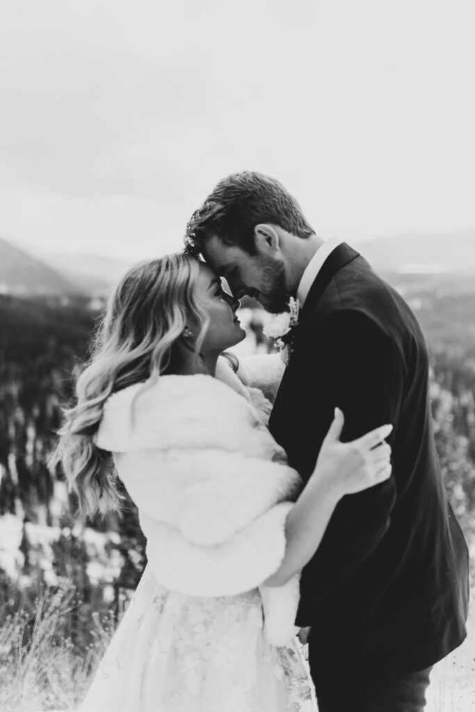 Black and white photo of bride and groom touching foreheads, smiling quietly during an intimate snowy mountaintop elopement